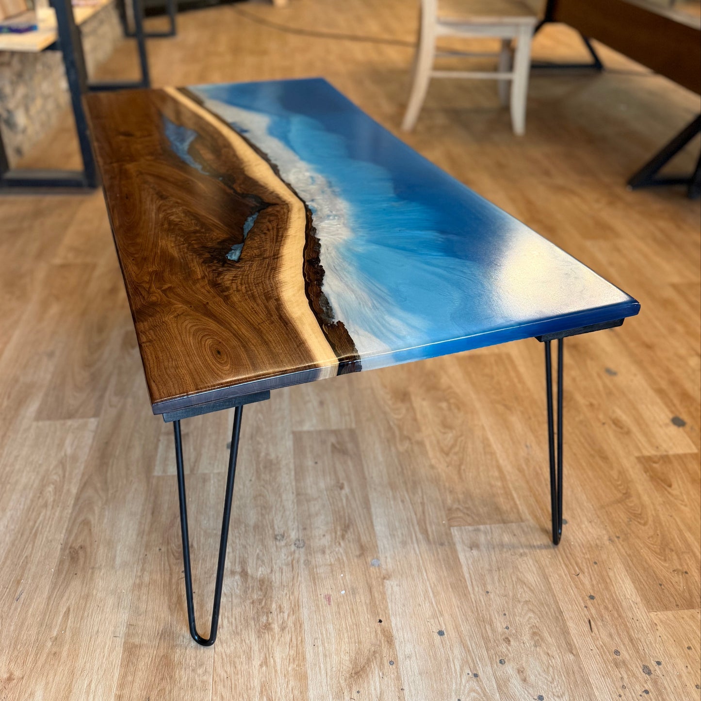 Table with blue resin waves design on a wooden floor in a room with other furniture.