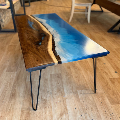 Table with blue resin waves design on a wooden floor in a room with other furniture.