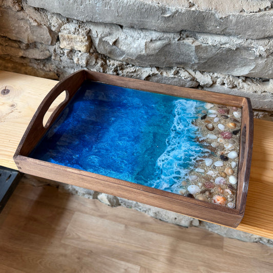 Wooden tray with a blue resin waves design on a stone wall background