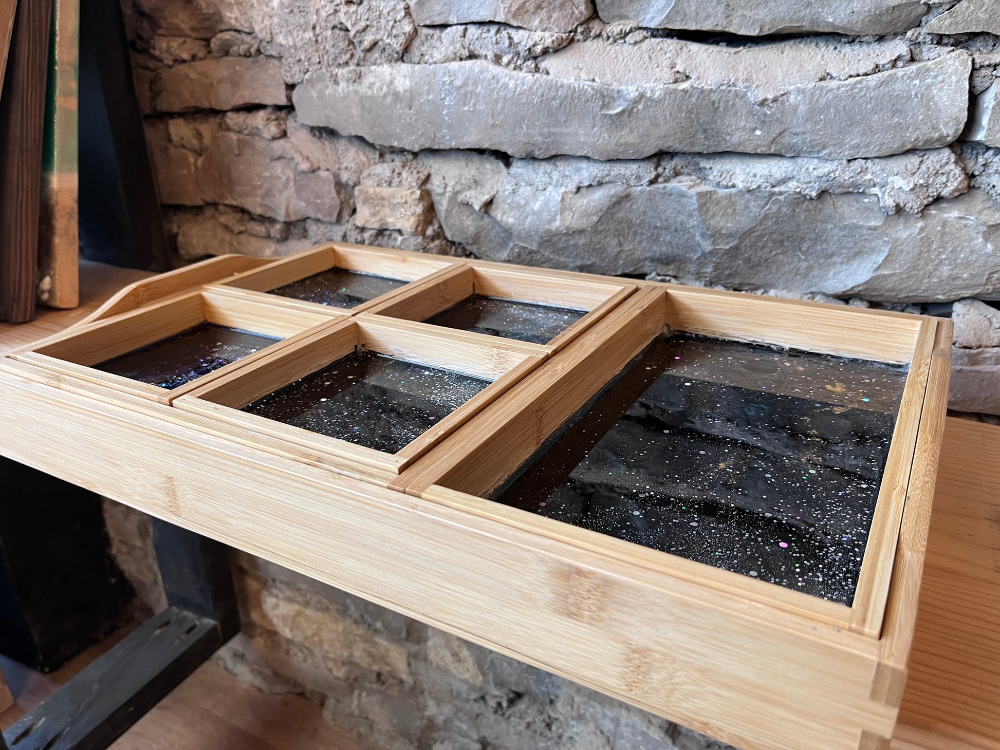 7-piece wooden charcuterie tray set with compartments and an epoxy galaxy design against a stone wall.