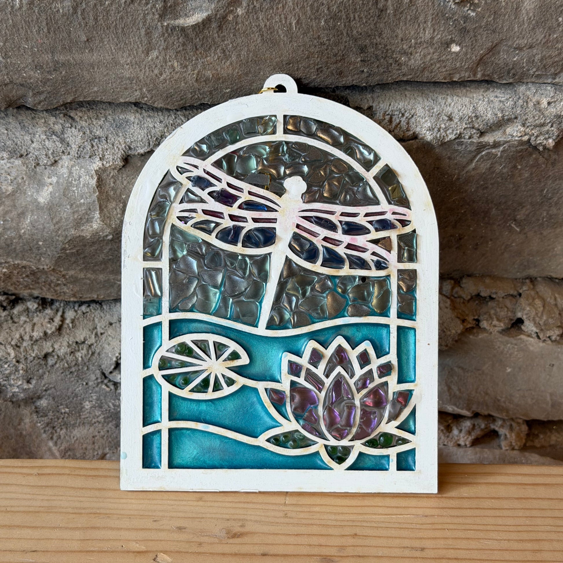 Suncatcher with a dragonfly and lotus design on a stone and wooden background