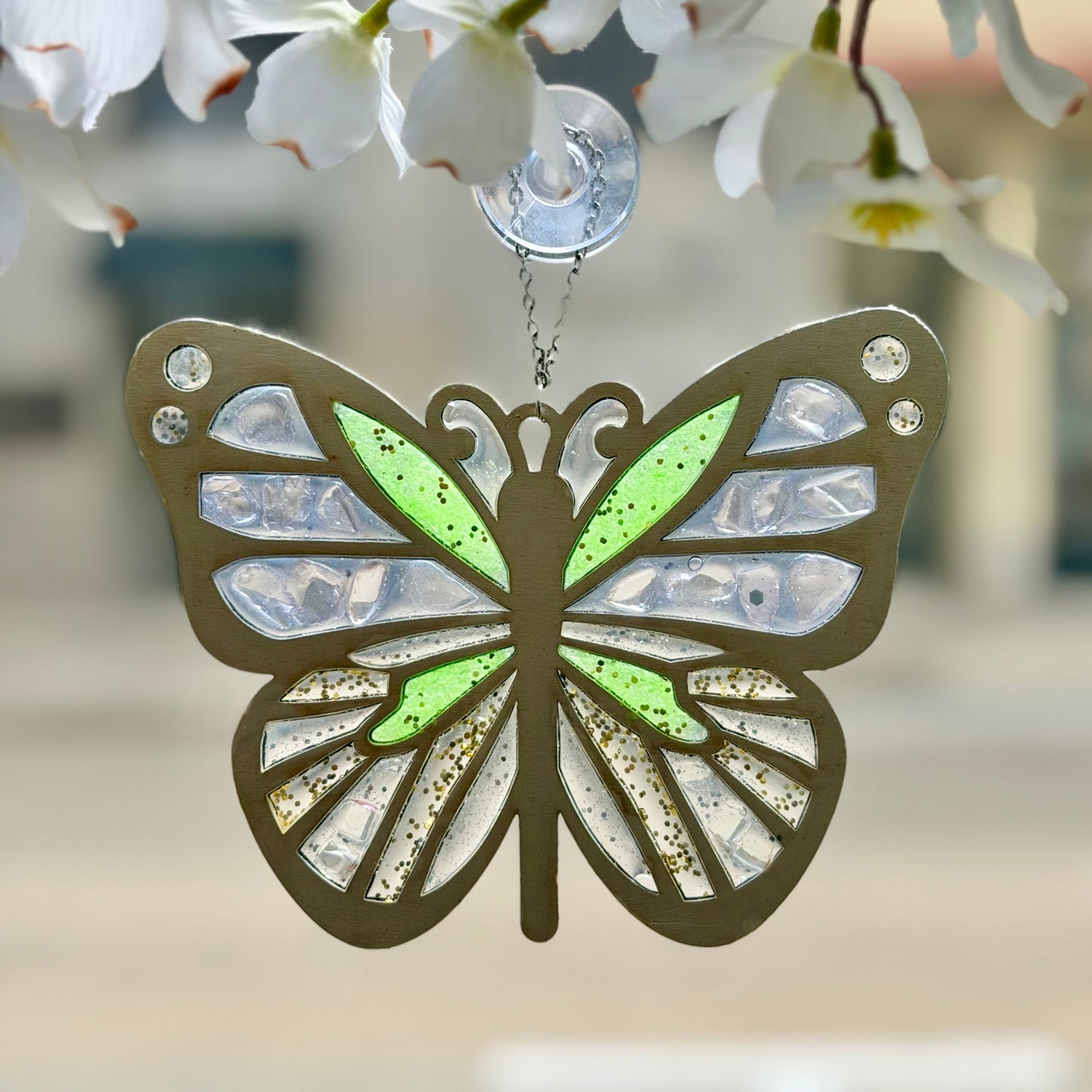 Butterfly-shaped suncatcher hanging against a blurred floral background.