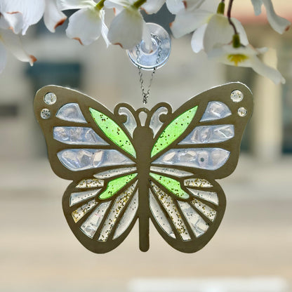 Butterfly-shaped suncatcher hanging against a blurred floral background.
