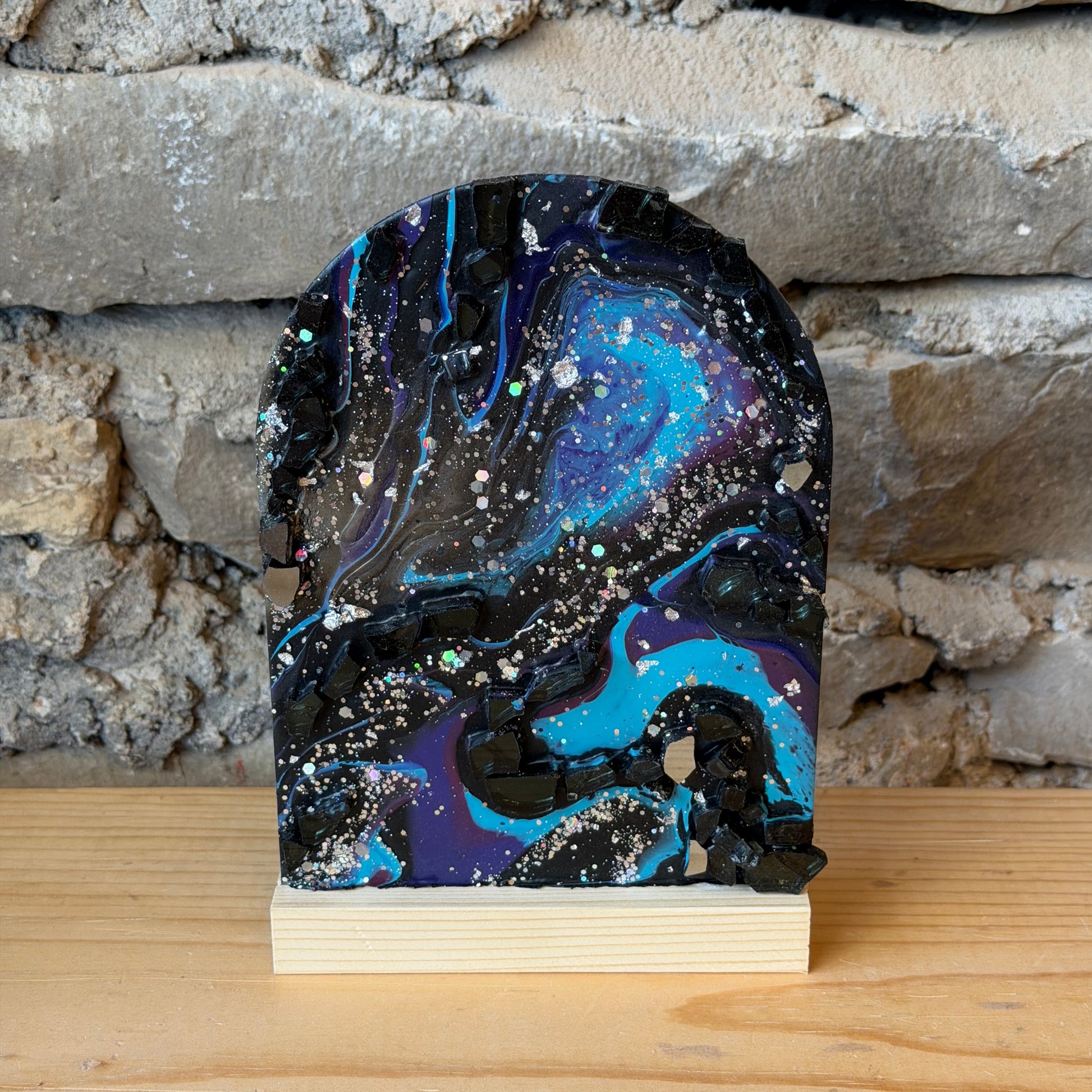 Decorative epoxy galaxy display with a blue and purple sky design attached to a wooden board against a stone wall.