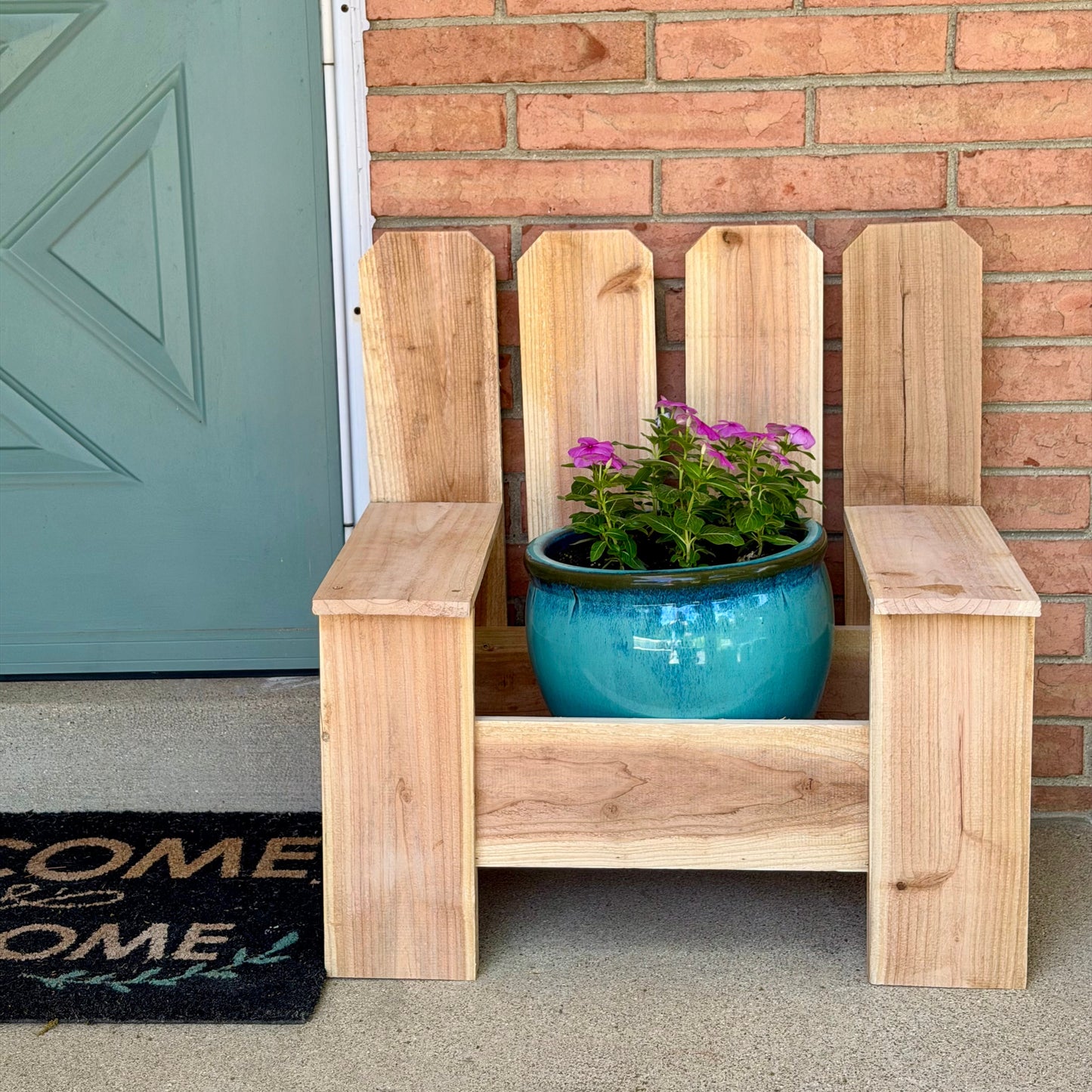 Wooden planter chair with a blue pot of flowers against a brick wall.