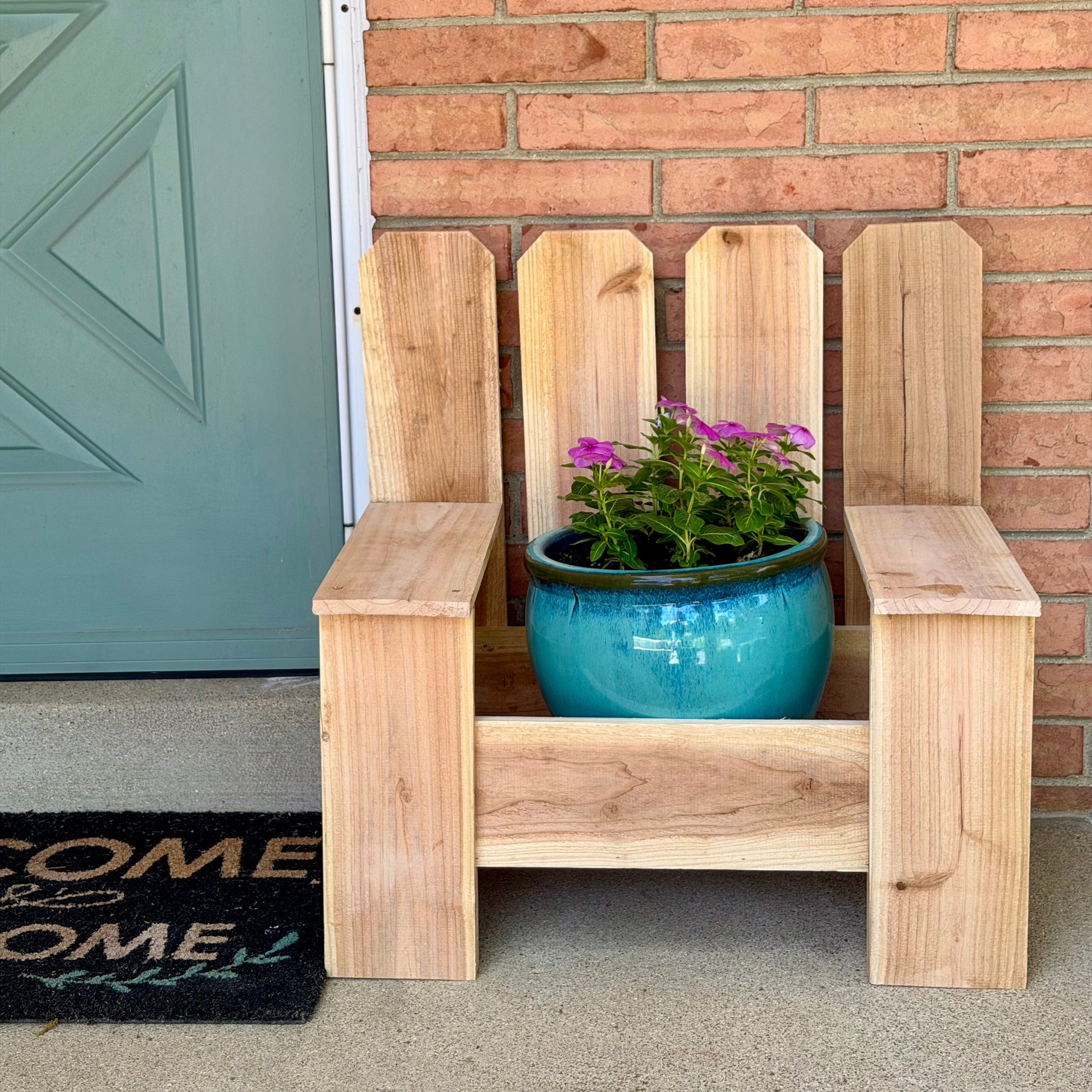 Wooden planter chair with a blue pot of flowers against a brick wall.