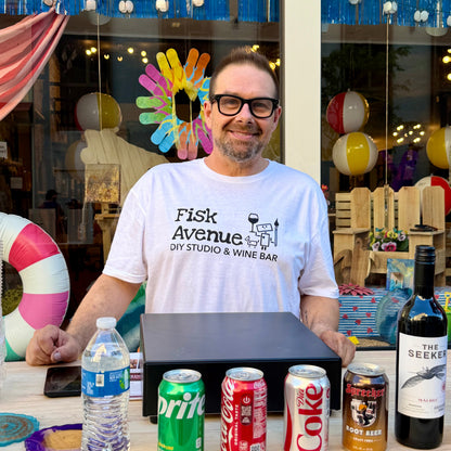 Man in a white t-shirt with a logo standing behind a counter with various drinks.