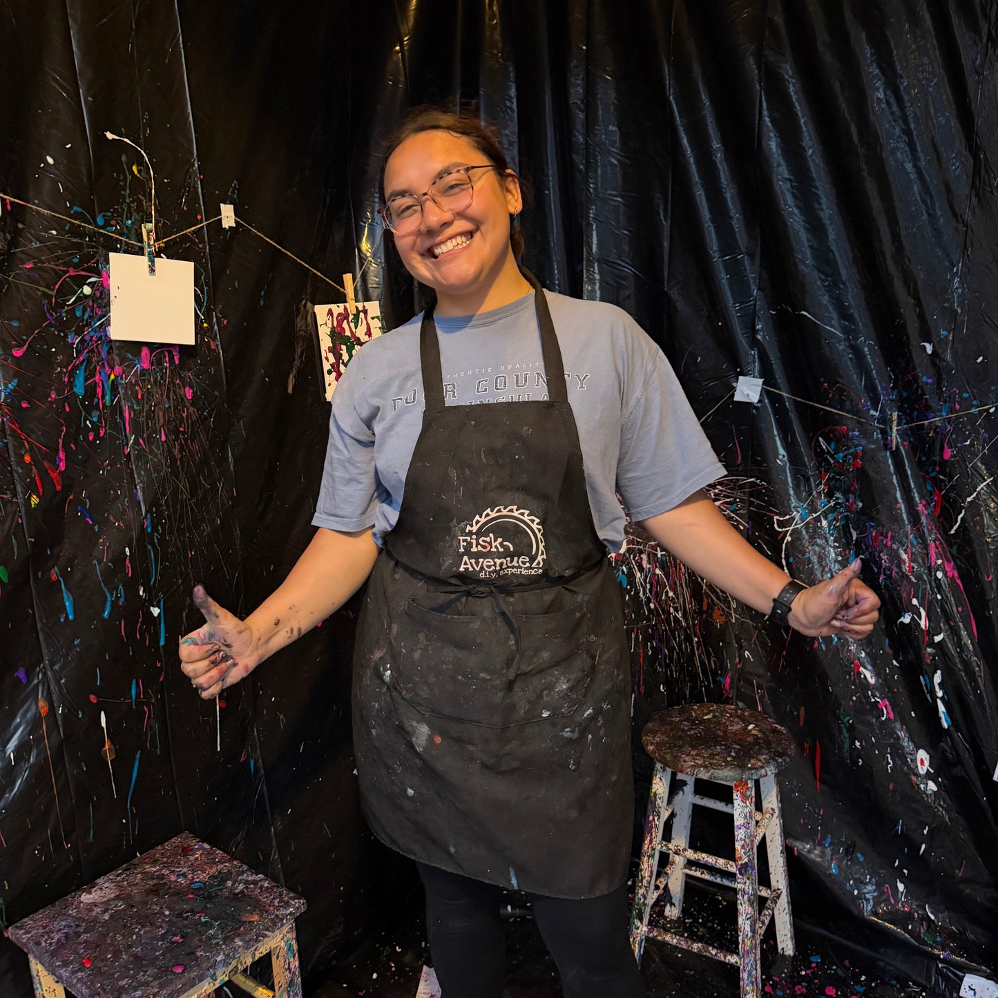 Instructor wearing an apron in a studio with art supplies and black curtains.