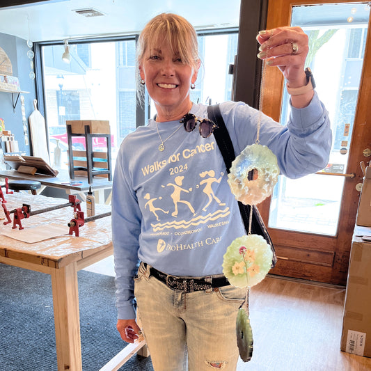 Person wearing a light blue sweatshirt with graphics and text, holding an epoxy geode suncatcher indoors.