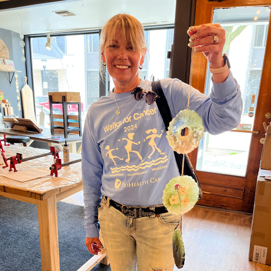 Woman holding a resin suncatcher, standing in a sutdio with a window and tables.