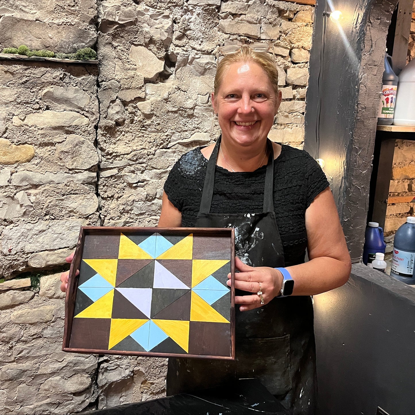 Person holding a geometric patterned tray against a stone wall.