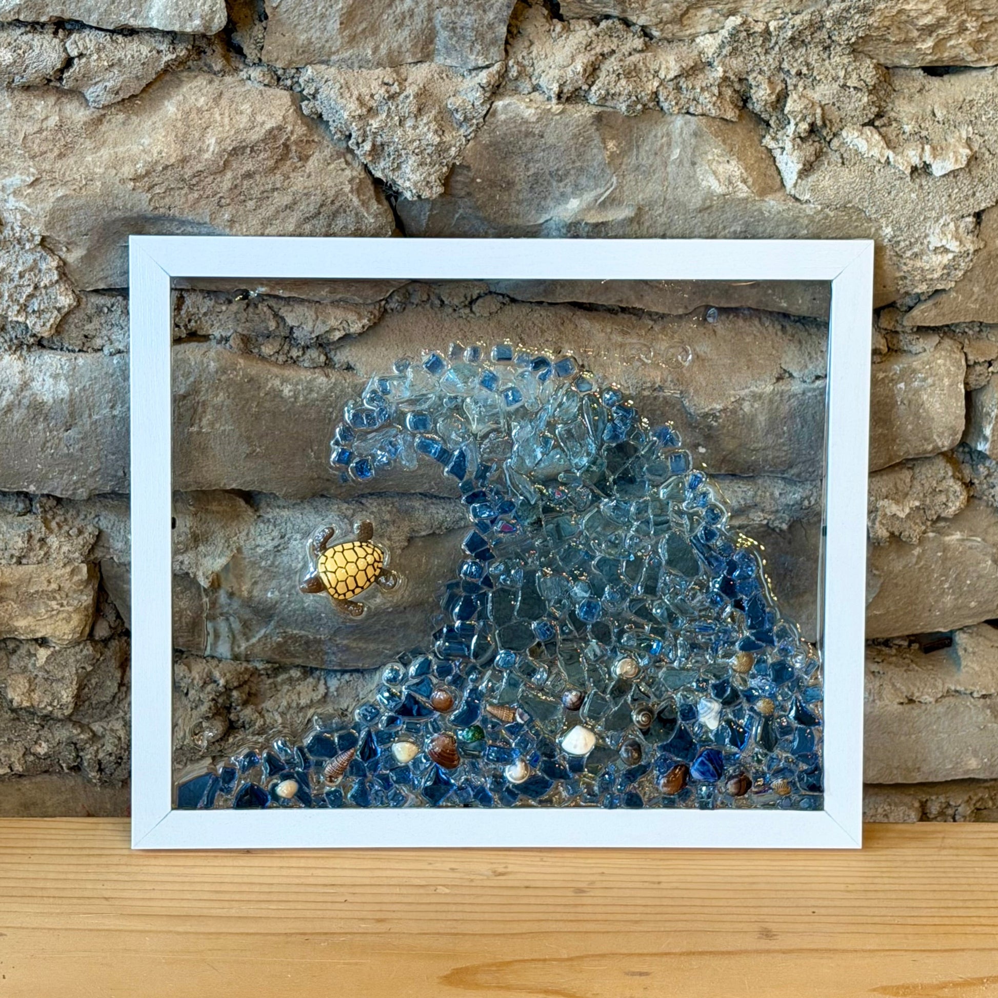 A framed glass art print depicting a blue ocean wave against a rustic stone wall.