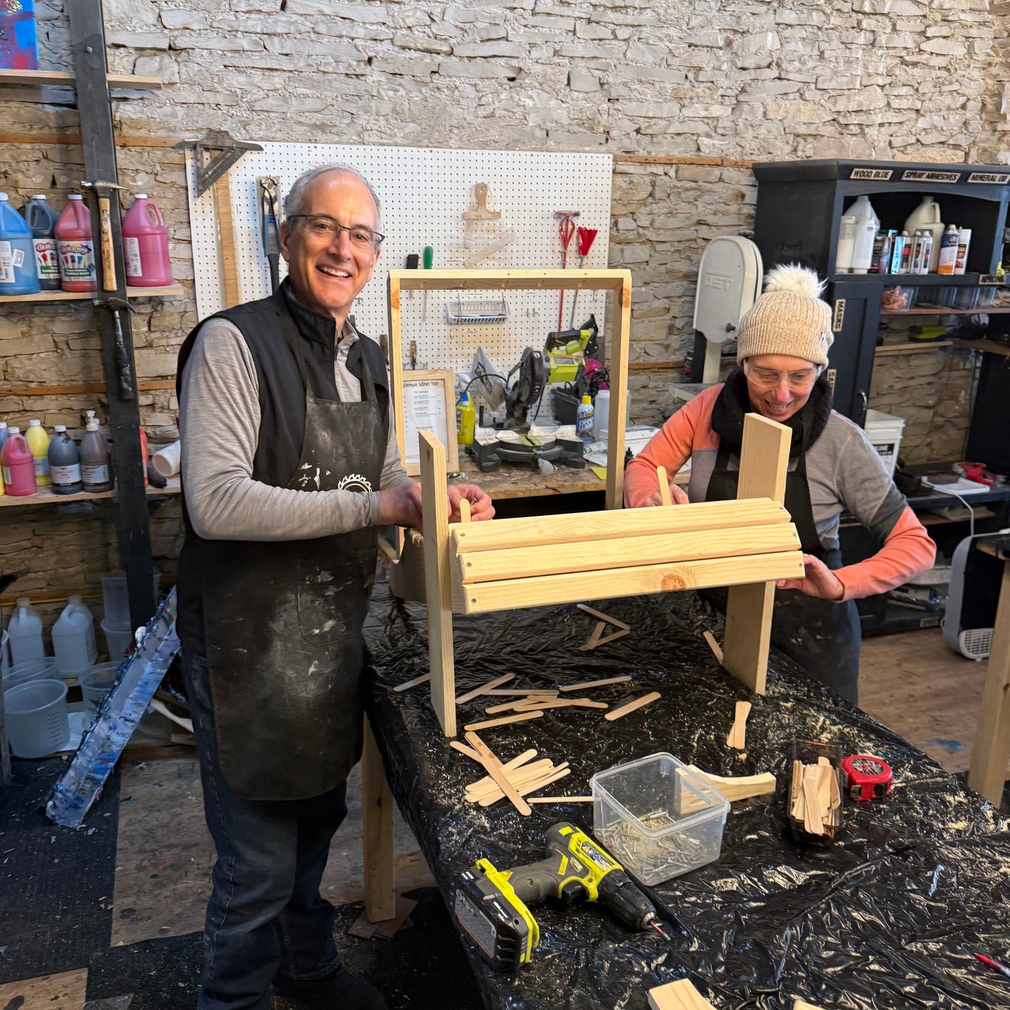 Two people working on a wooden chiar project in a workshop setting.