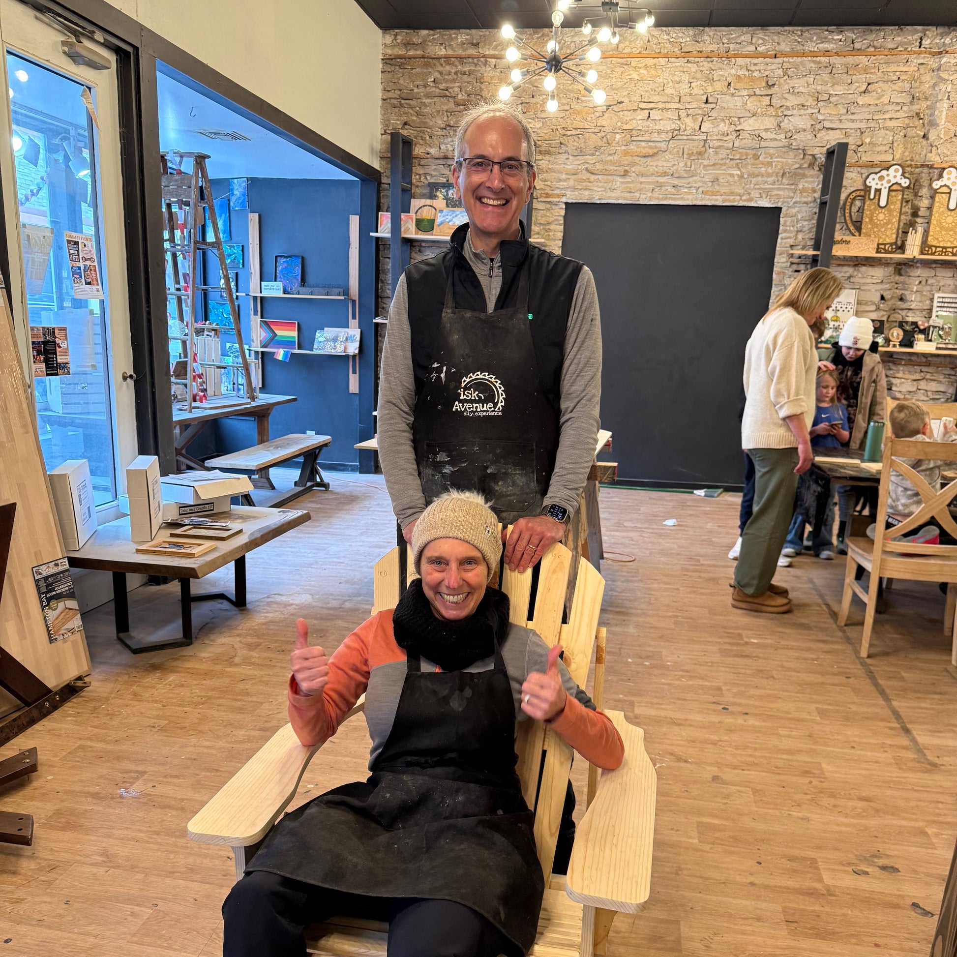 Two people smiling in a studio with their handmade Adirondack chair.
