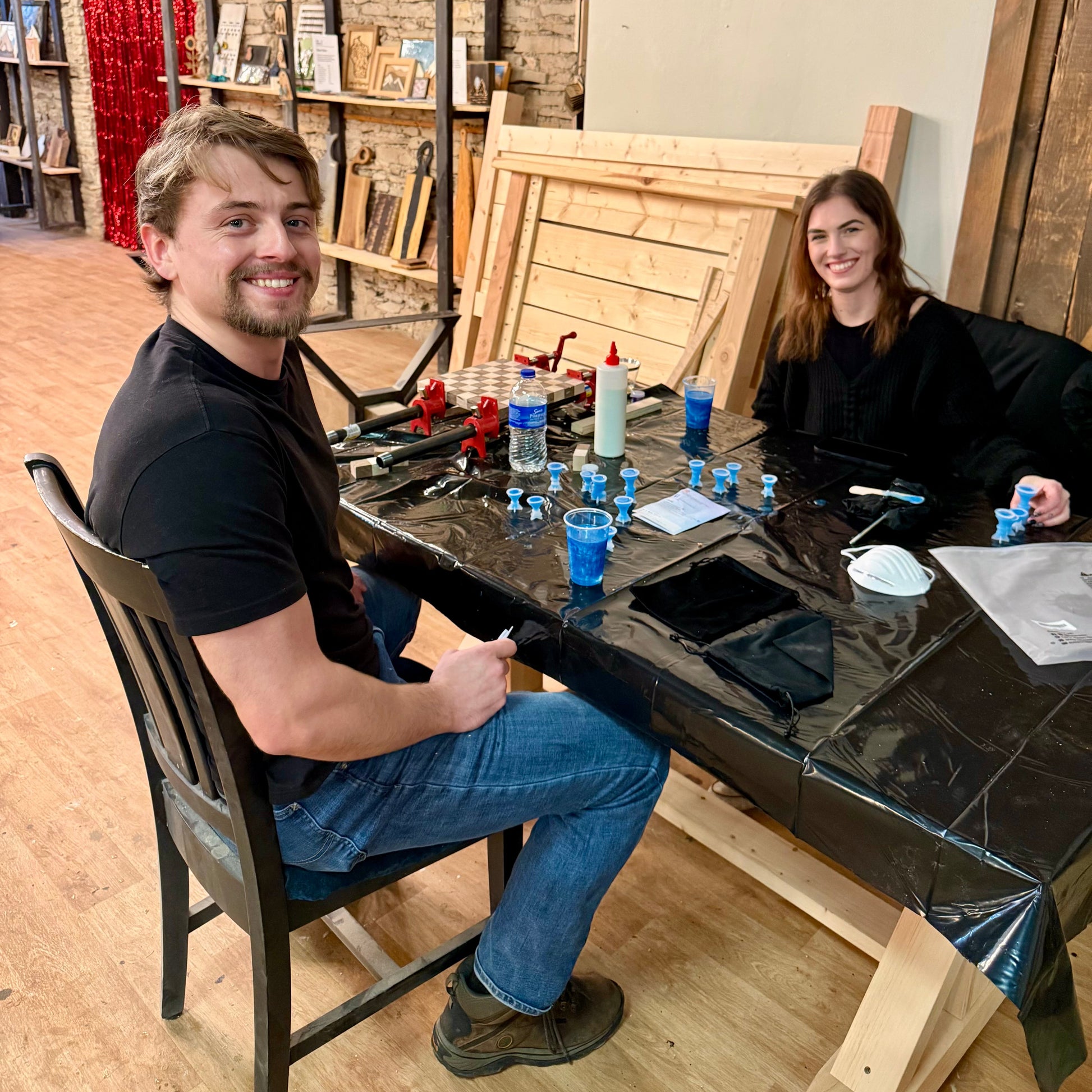 Two people sitting at a table with molds for epoxy chess pieces in a workshop setting.
