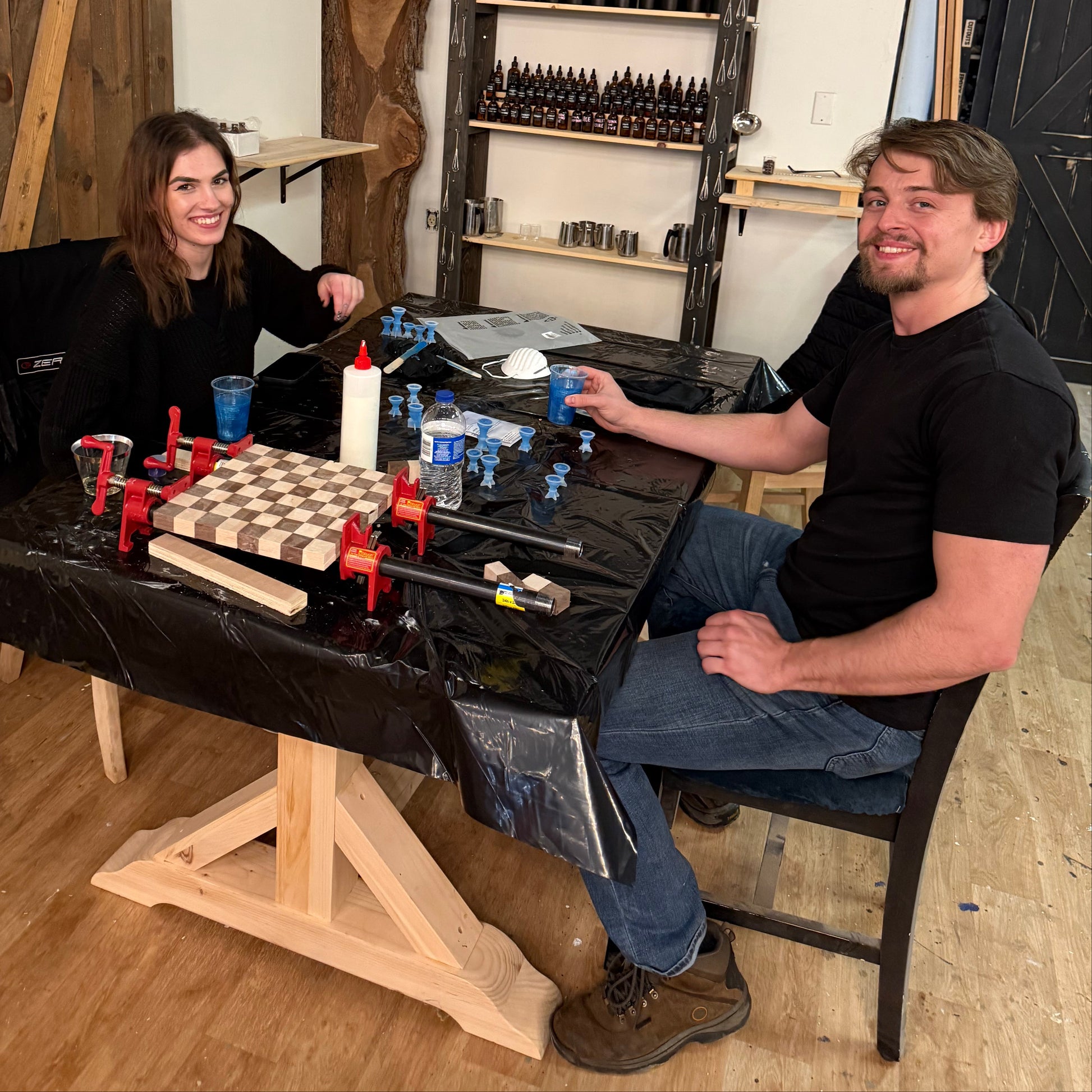 Two people working on a wooden chess board in a workshop.