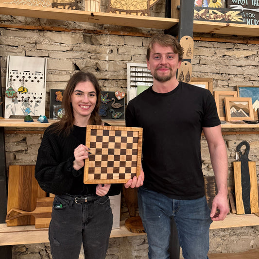 Two people standing in a studio with their handmade wooden chess board.