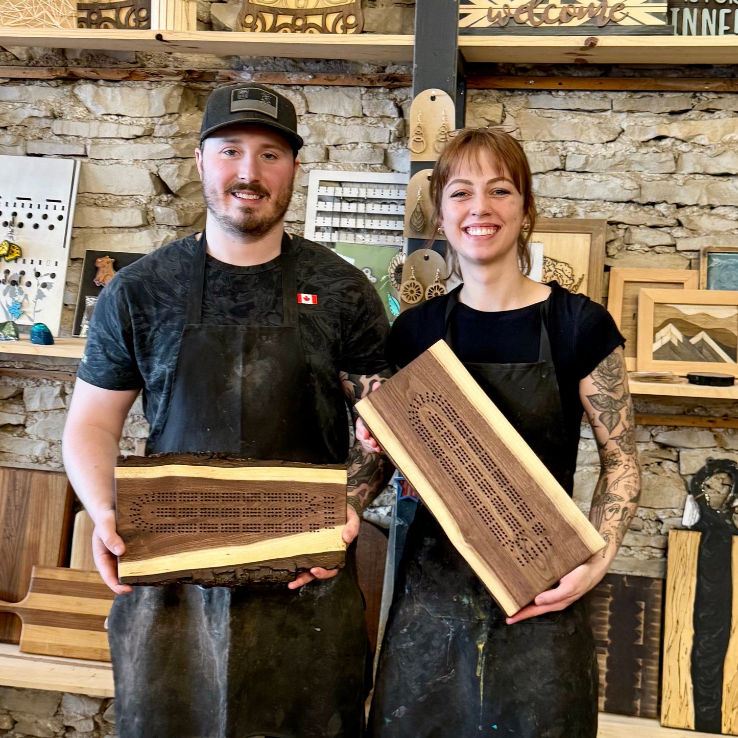 Two people holding wooden cribbage boards in a workshop setting