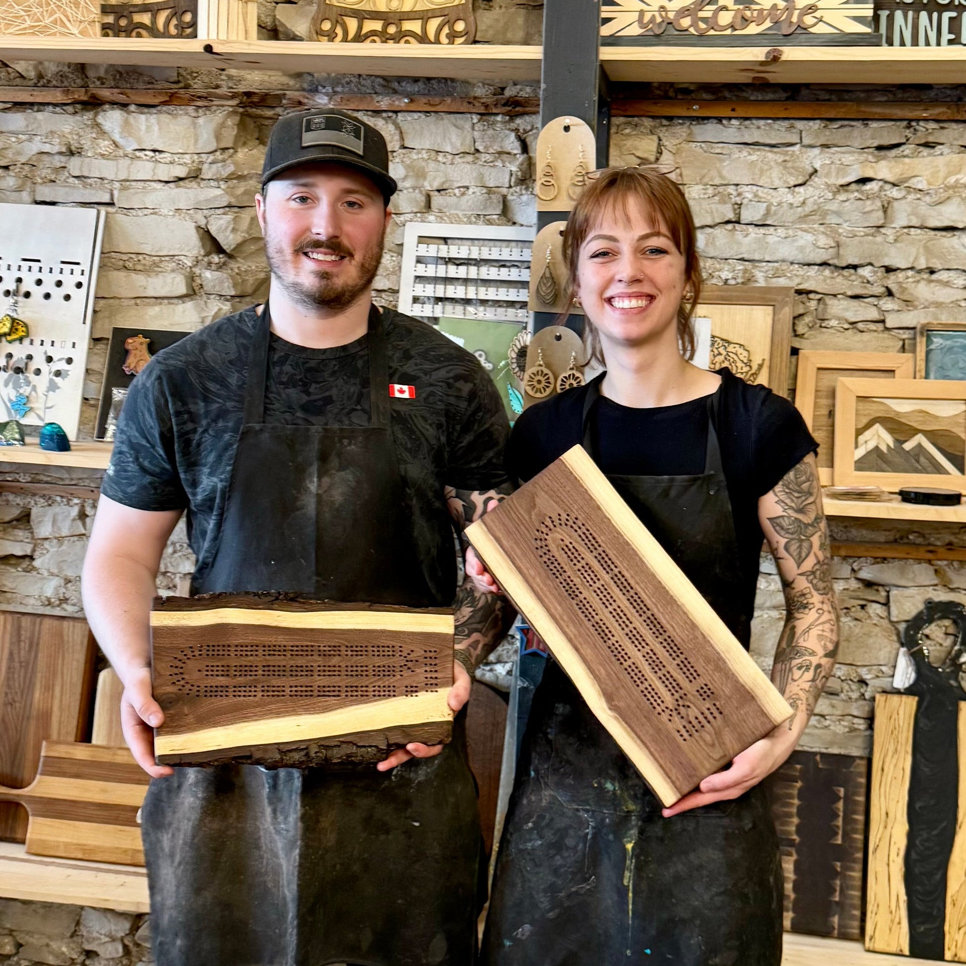Two people holding wooden cribbage boards in a workshop setting