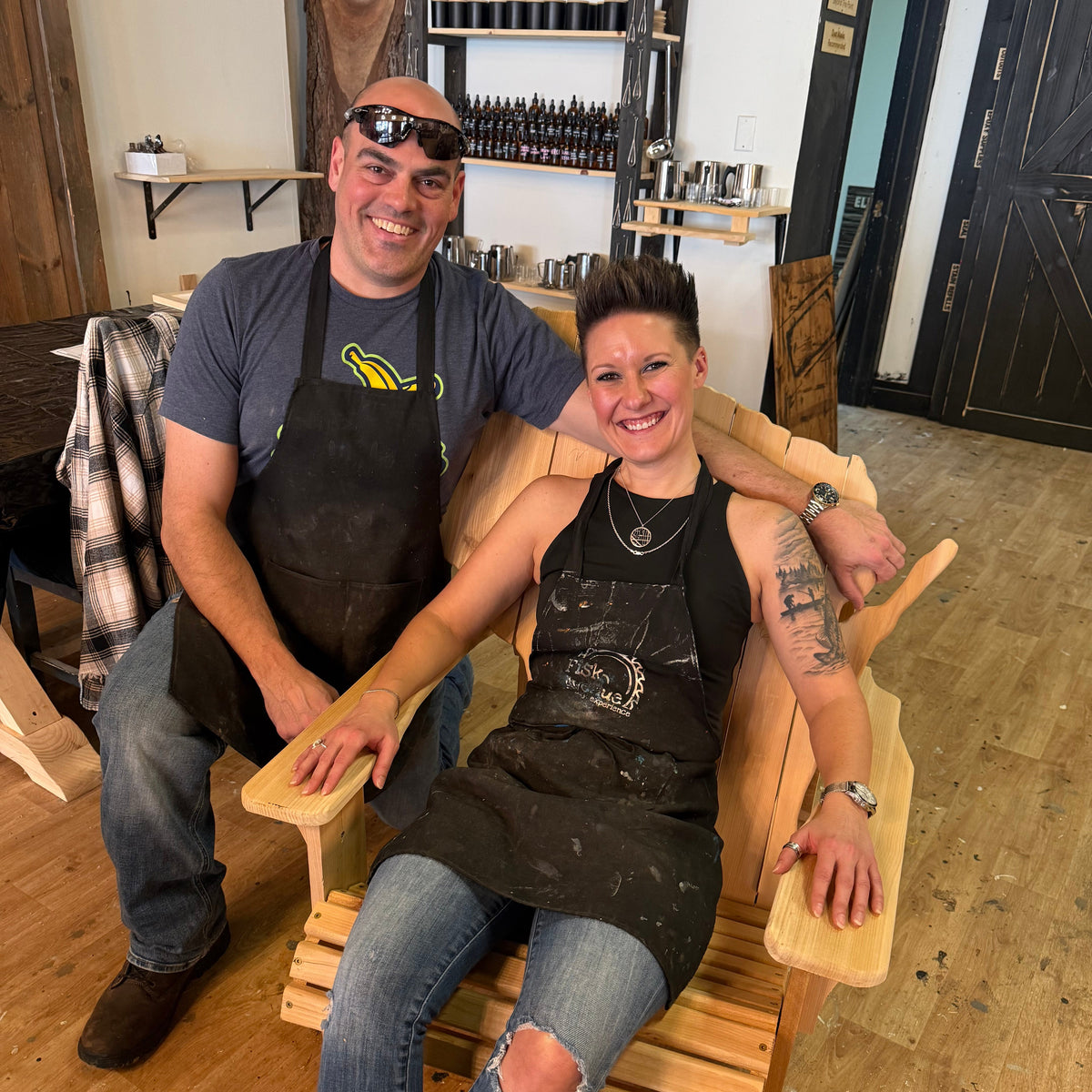 Two people sitting on a wooden Wisconsin adirondack chair in a workshop setting.