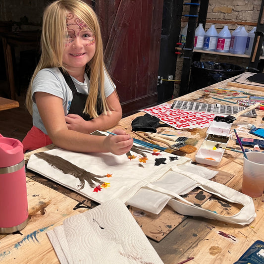 Child sitting at a table with art supplies and a trick-or-treat tote bag.