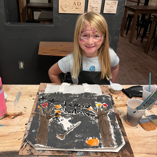 Person in a workshop with art supplies and a painted trick-or-treat tote bad on a table.
