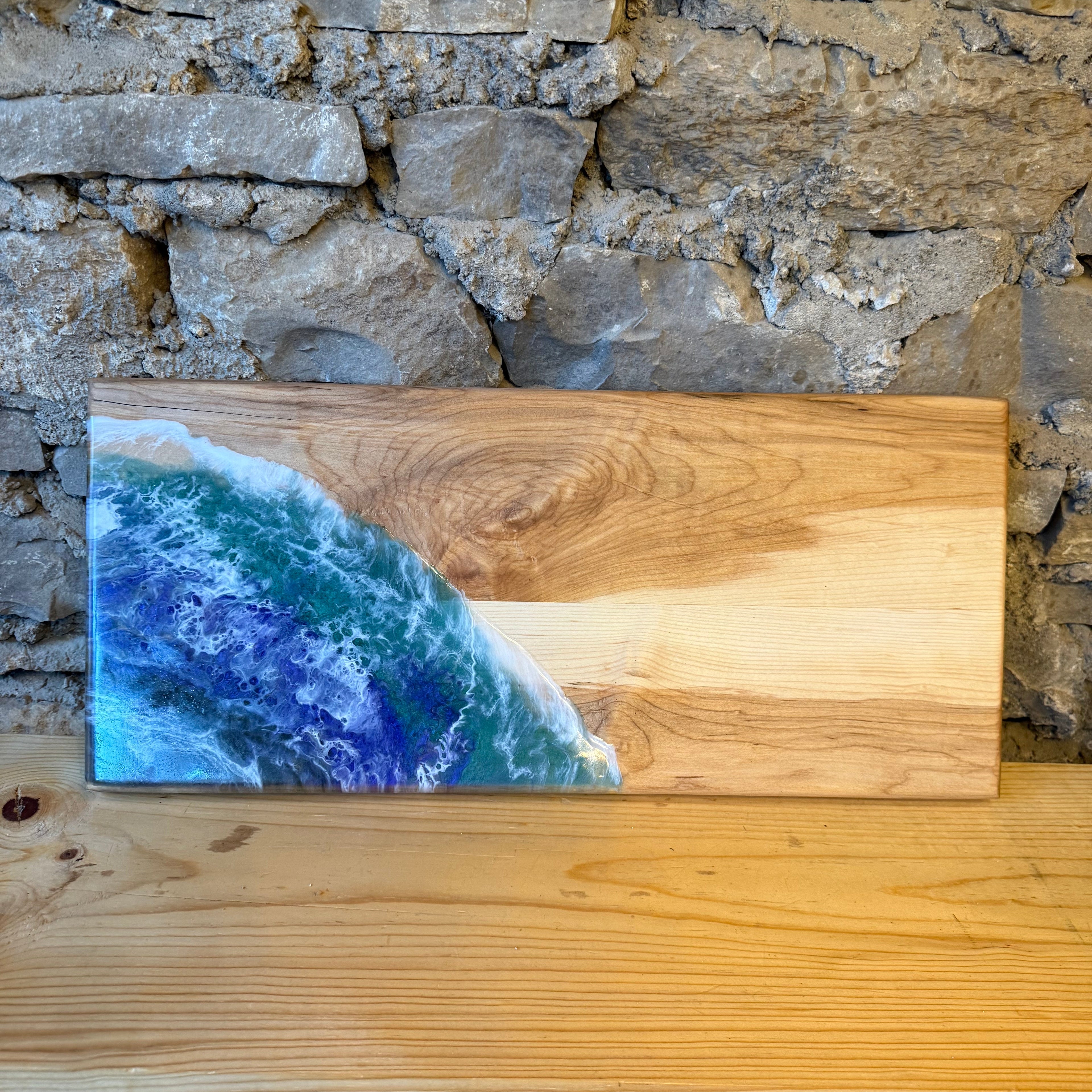 Wooden board with a resin design of ocean waves against a stone wall.