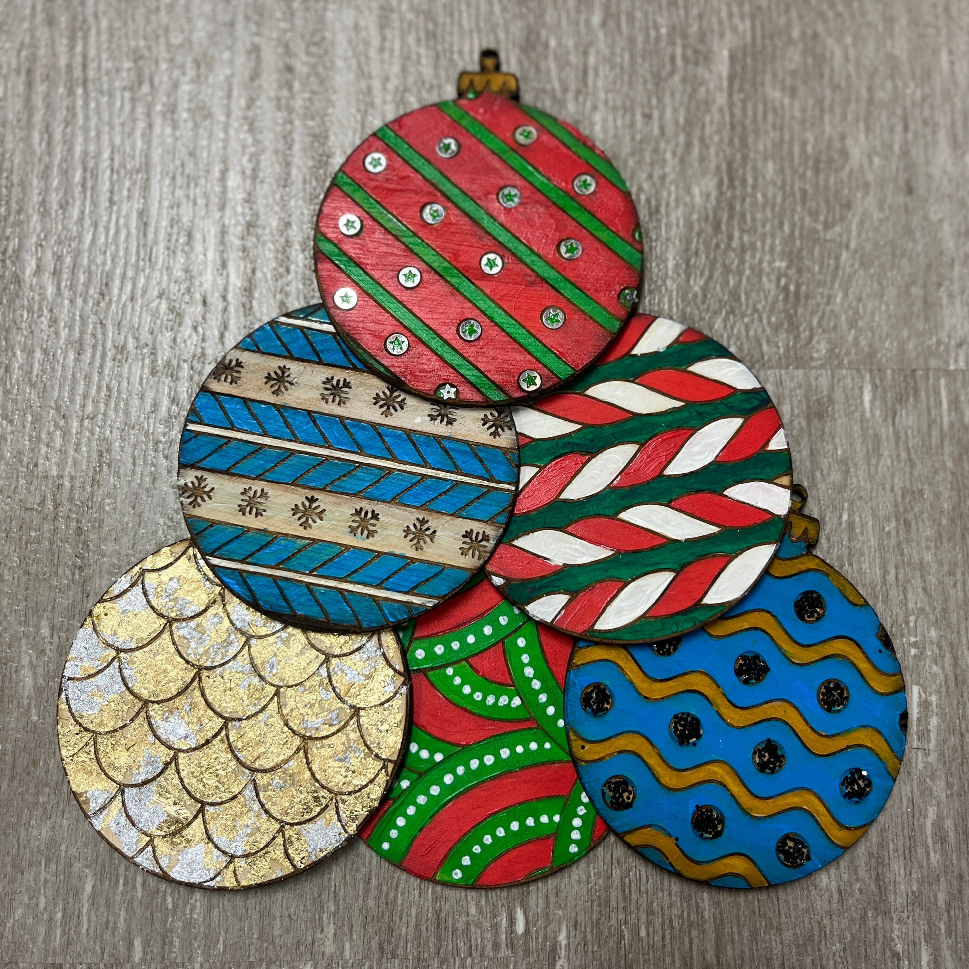 A selection of engraved wooden Christmas ornaments with a variety of colors and patterns, including solid colors and geometric designs.