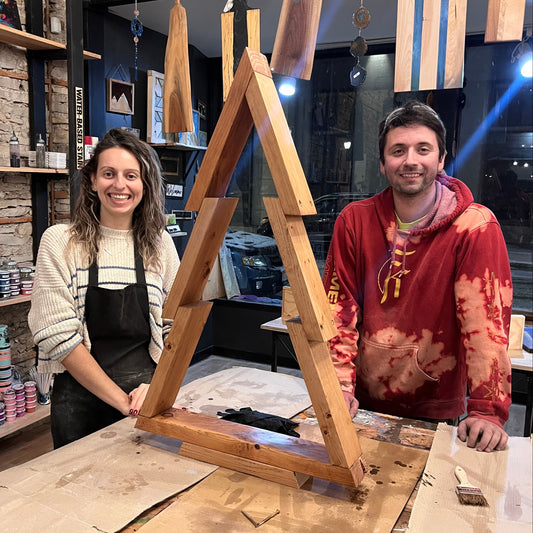 Two people standing behind a wooden tree project in a workshop setting.