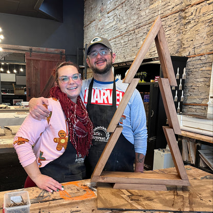 Two people standing in a studio room with a wooden tree project.
