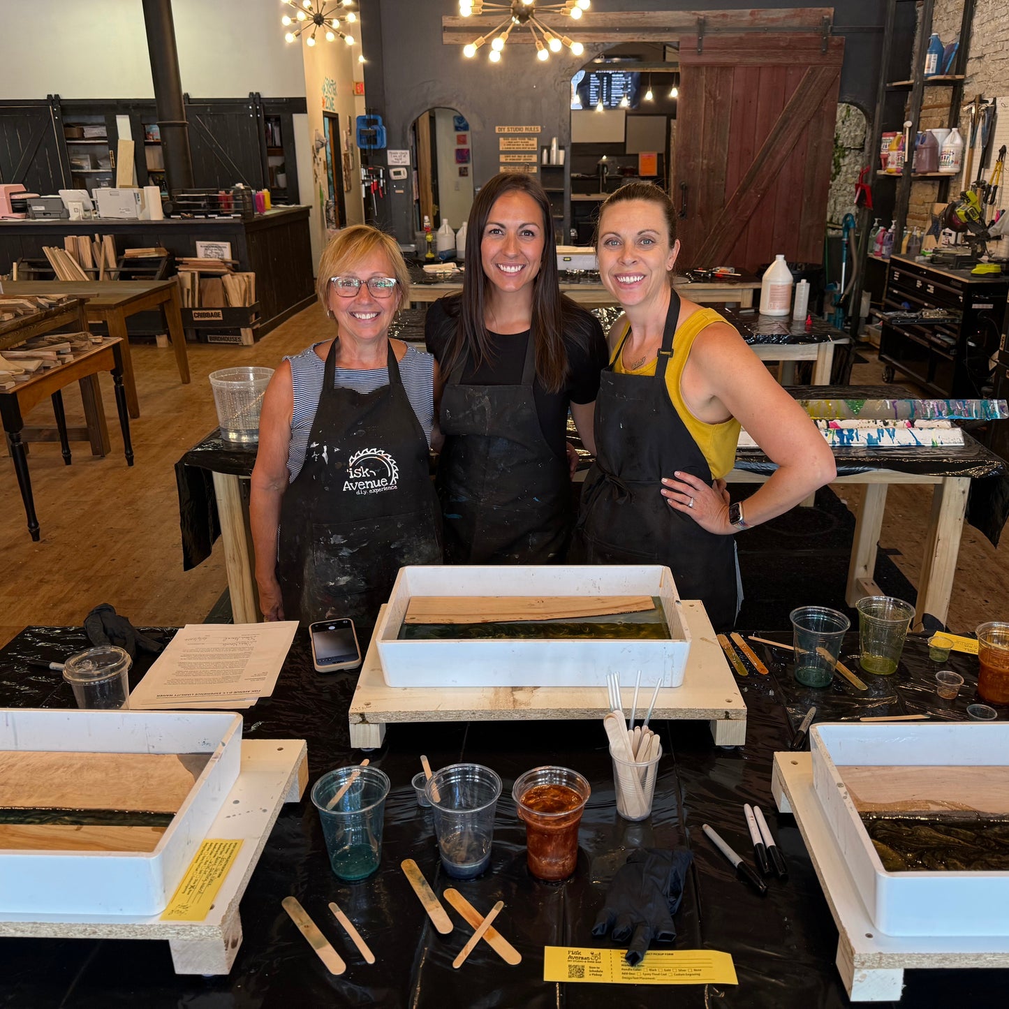 Three women in a studio making epoxy river serving trays.