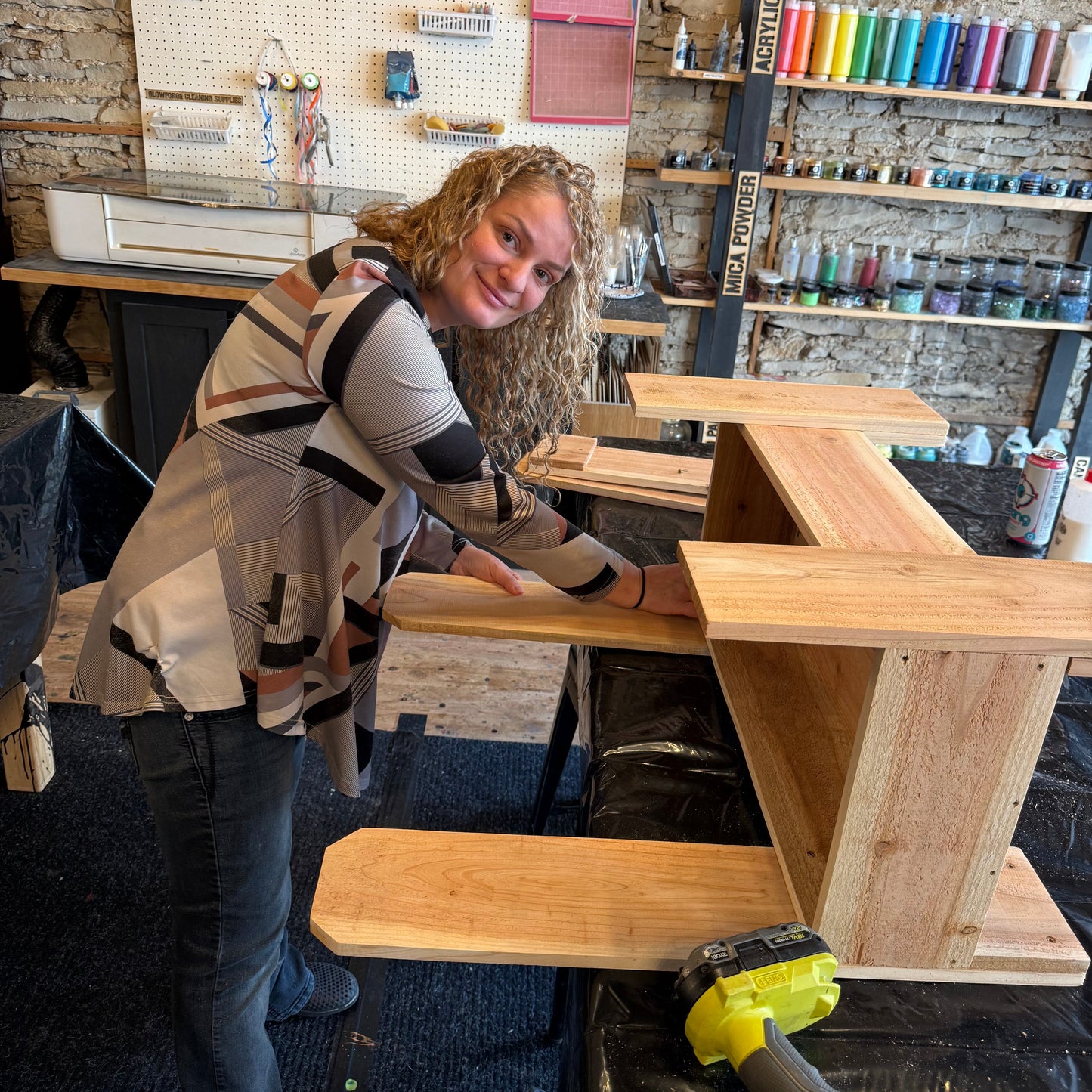Person working on a wooden planter project in a workshop with tools and materials around.