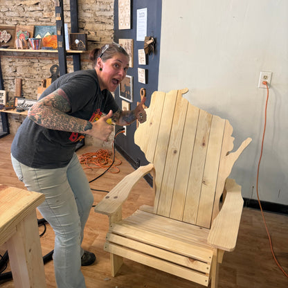 Person working on a wooden chair shaped like the state of Wisconsin in a workshop.