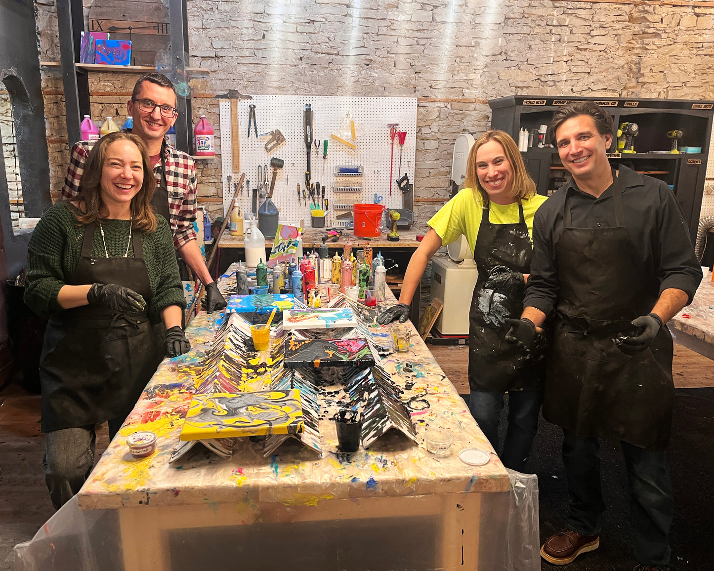 Four people in a workshop setting with art supplies on a table.