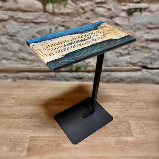 Small table with a cribbage game surface on a wooden floor against a stone wall background
