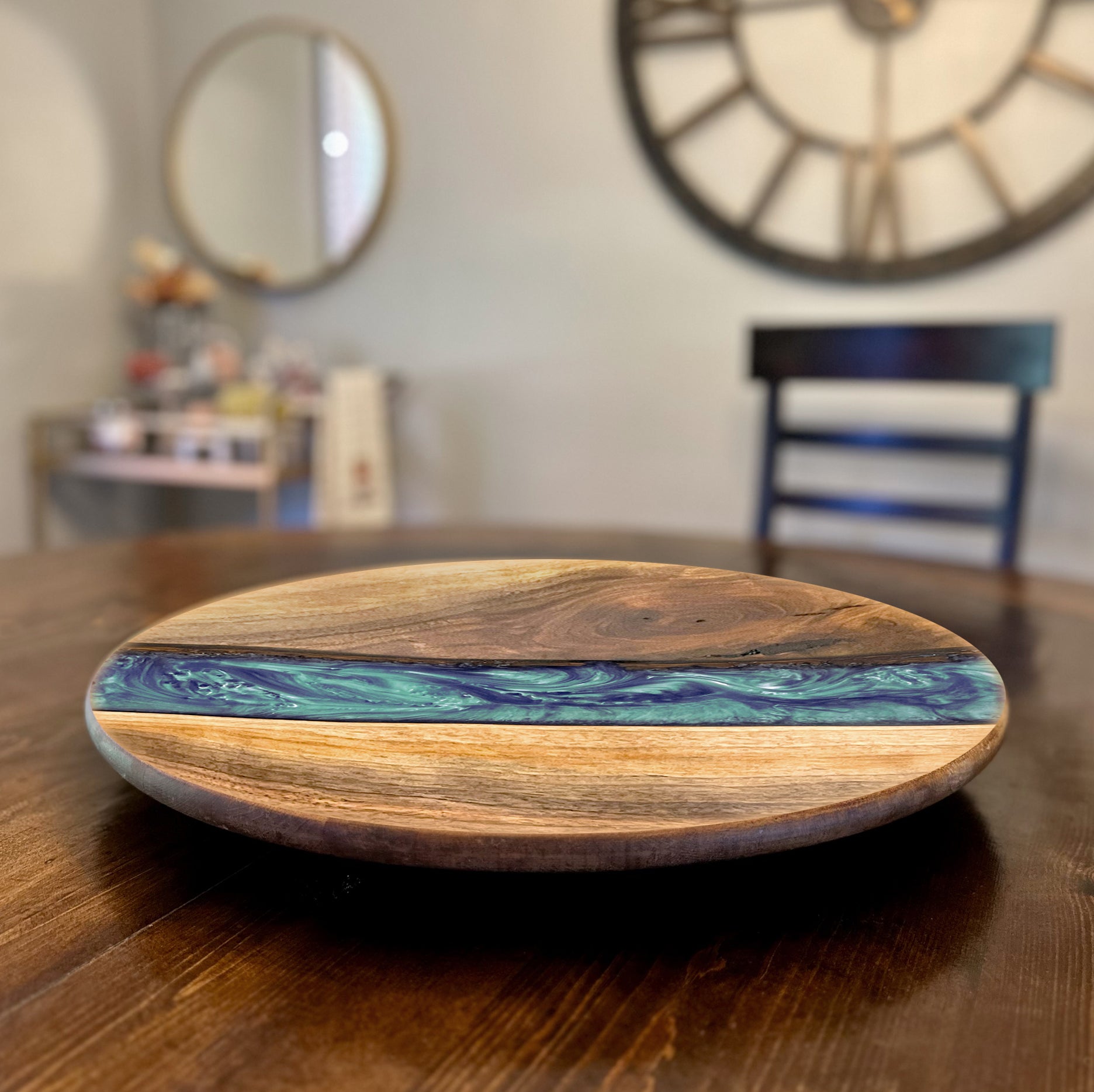 Wooden lazy susan turntable board with a blue and green epoxy design on a wooden table.