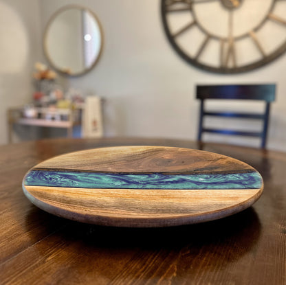 Wooden lazy susan turntable board with a blue and green epoxy design on a wooden table.