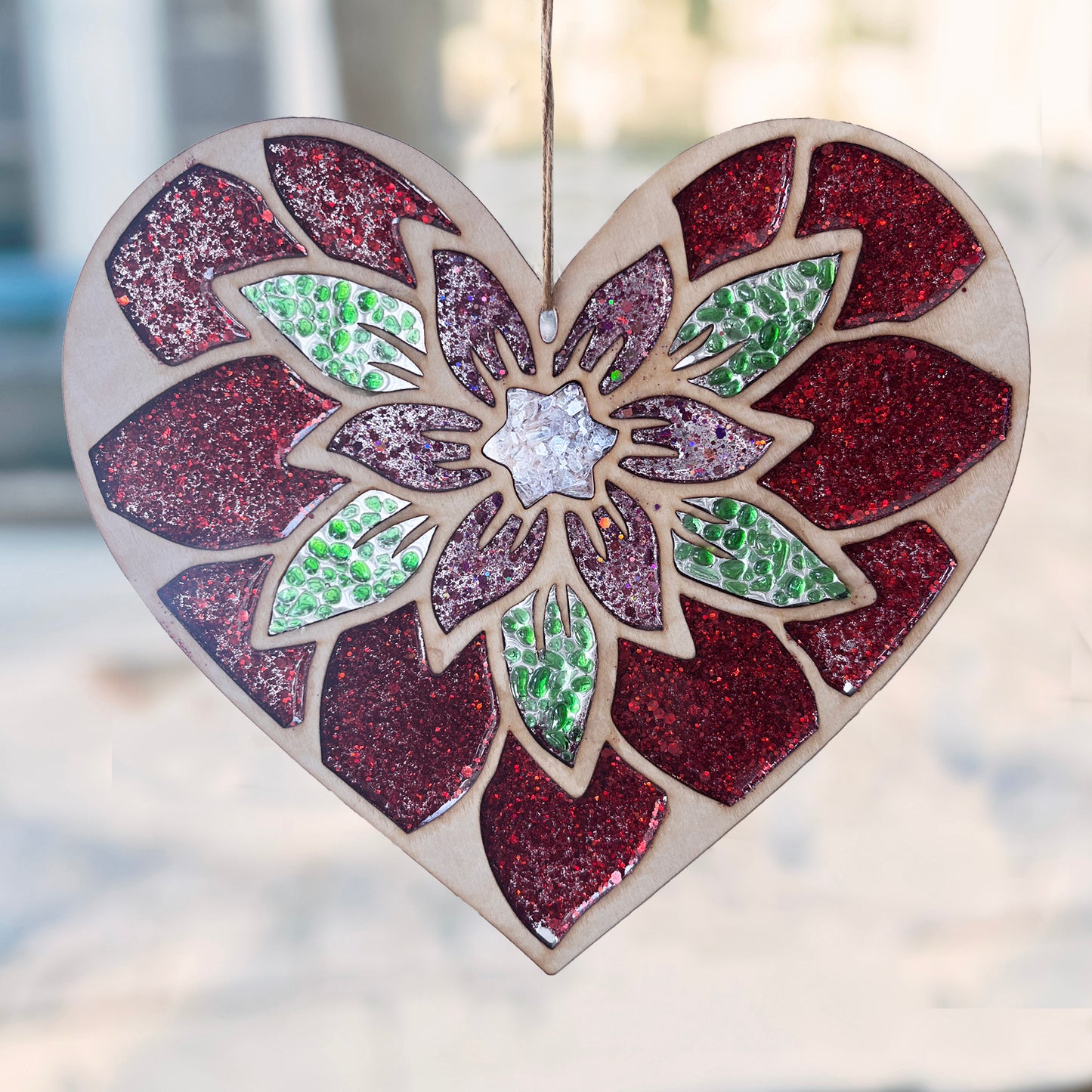 Heart-shaped suncatcher with a floral design and glittery finish, hanging against a blurred street scene.