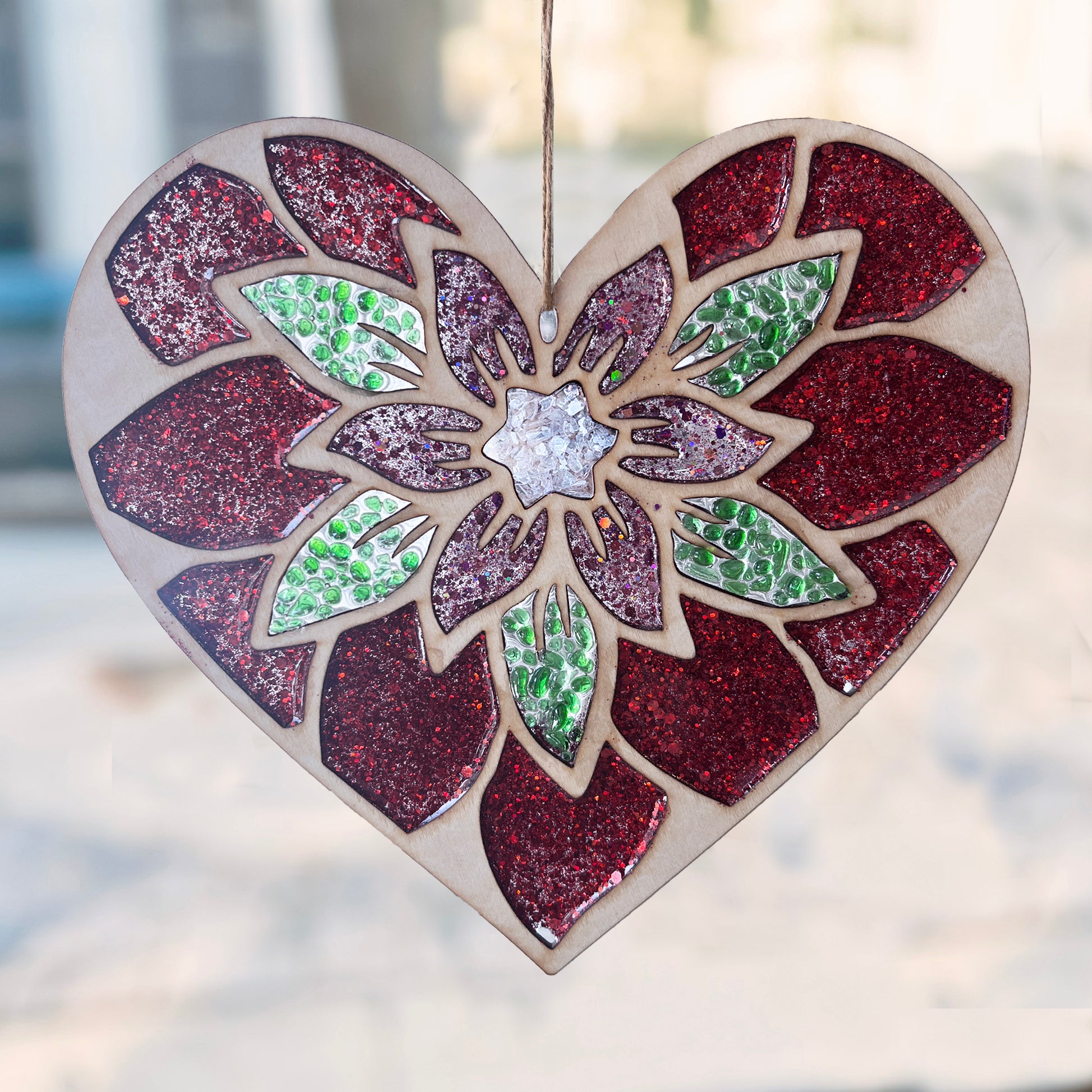 Heart-shaped suncatcher with a floral design and glittery finish, hanging against a blurred street scene.