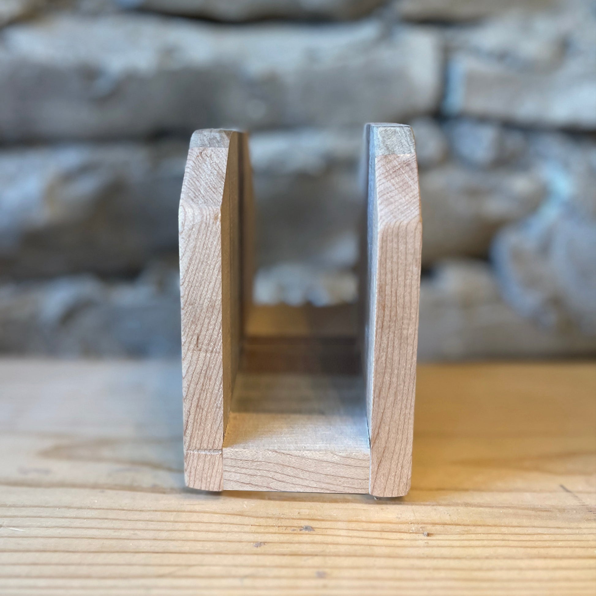 Wooden napkin holder on a wooden surface with a stone wall background
