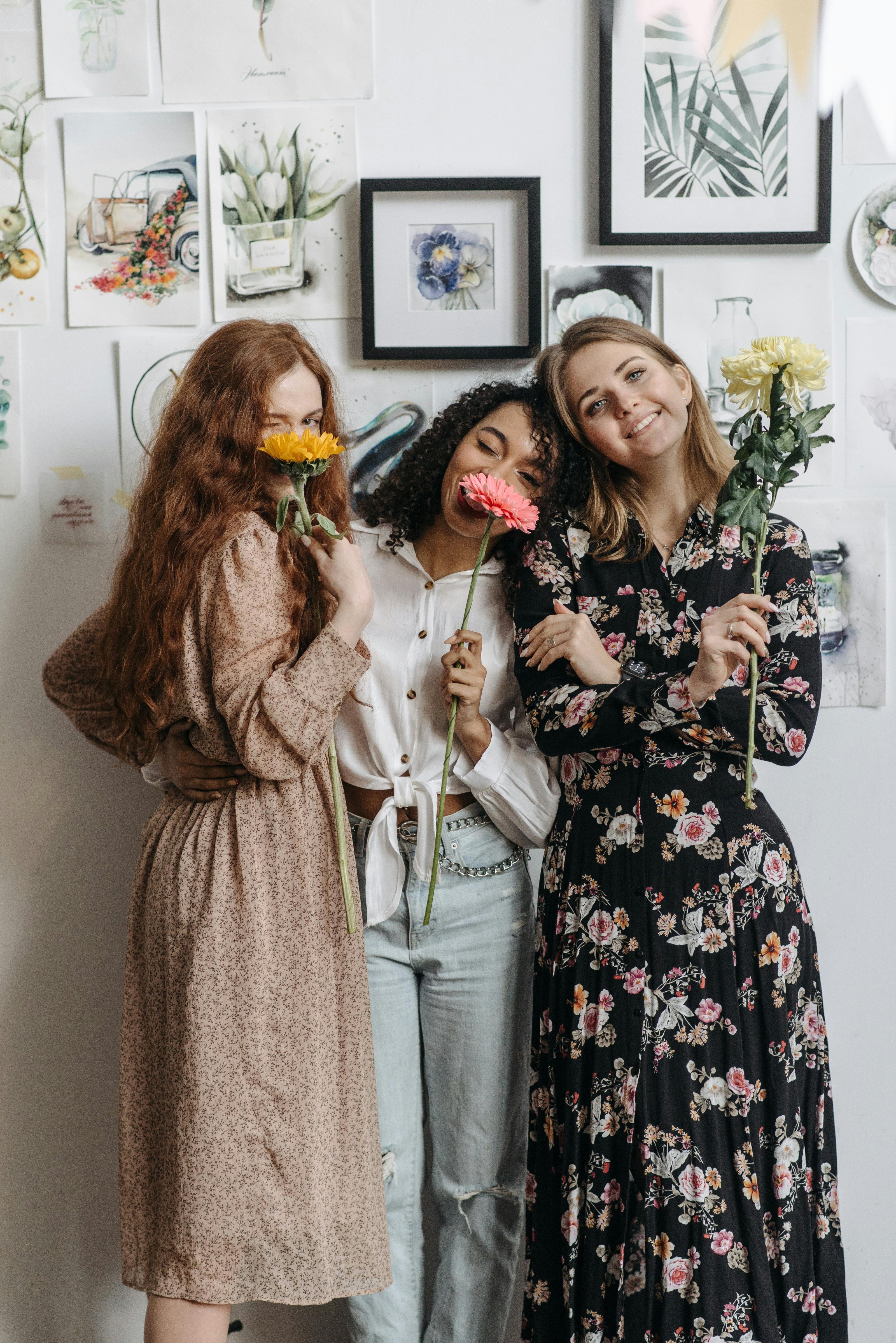 Three women holding flowers by a while wall with painted artwork