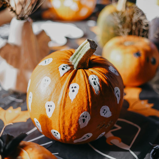 Decorative pumpkin with ghost patterns on a Halloween-themed tablecloth.